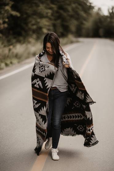Une femme sur une route déserte est enveloppée d’une couverture ornée de motifs traditionnels autochtones.