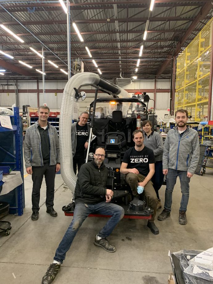 Un groupe d’employés de l’équipe d’ingénierie d’Exprolink pose autour d’un véhicule Madvac électrique vêtu de t-shirts de l’entrepris de batteries électriques Zero.