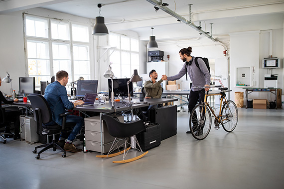 Des employés d'une entreprise de développement logiciel saluent un collègue qui arrive avec son vélo