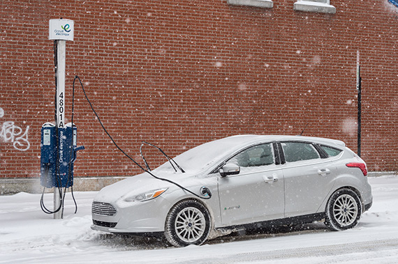 Une voiture électrique branchée à une borne de recharge durant une tempête de neige