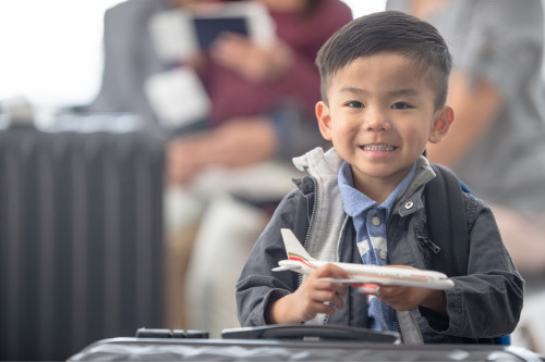 Un petit garçon d’environ trois ans tient un avion jouet dans ses mains en attendant de prendre son vol. 
